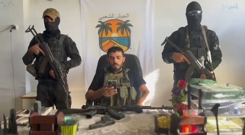  أشرف المنسي، قائد ميليشيا الجيش الشعبي يجلس بين مسلّحَين. (وكالة معاً)