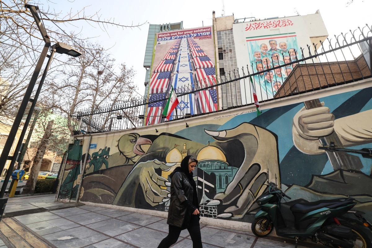 امرأة إيرانية تمر أمام لافتة مناهضة للولايات المتحدة وإسرائيل في طهران (أ ف ب)