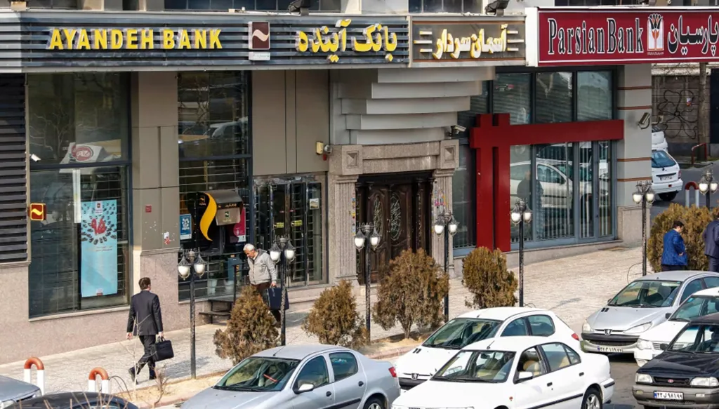 إيرانيون يمرون أمام أحد فروع بنك «آينده» (أرشيفية - أ.ف.ب)