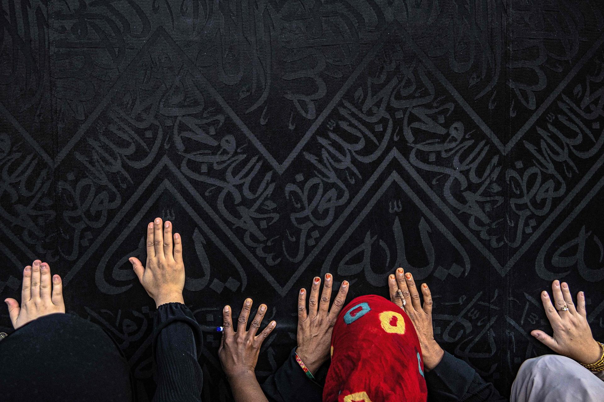 أيدٍ تلامس كسوة الكعبة، فيما تظهر الزخارف والآيات المنسوجة بخيوط دقيقة على الحرير الأسود (أ ف ب).