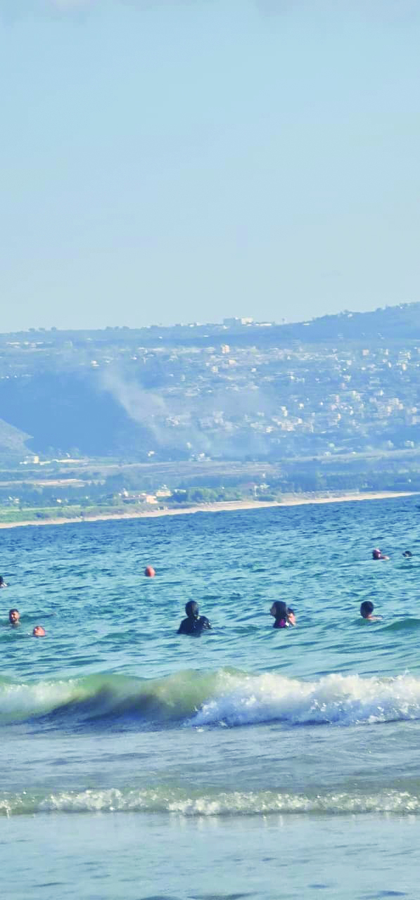 مواطنون يمارسون هواية السباحة على شاطئ صور فيما يتصاعد الدخان قبالتهم جراء قصف إسرائيلي جنوب المدينة (صورة متداولة)