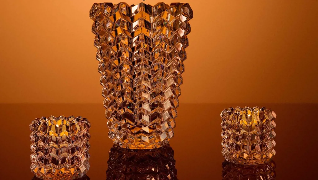 مزهرية II Eye من الكريستال، بتصميم يرتكز على تداخل الزوايا المصقولة، ما يمنح القطعة تأثيراً بصرياً يخدع النظر. يمكن تنسيقها مع شموع من "باكارا" لتشكيل طقم متكامل.