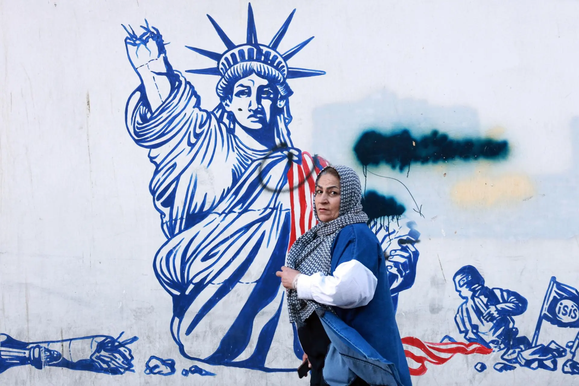 امرأة تمرّ أمام رسم جداري في طهران يصوّر تمثال الحرية مشوّهاً (أ ف ب)