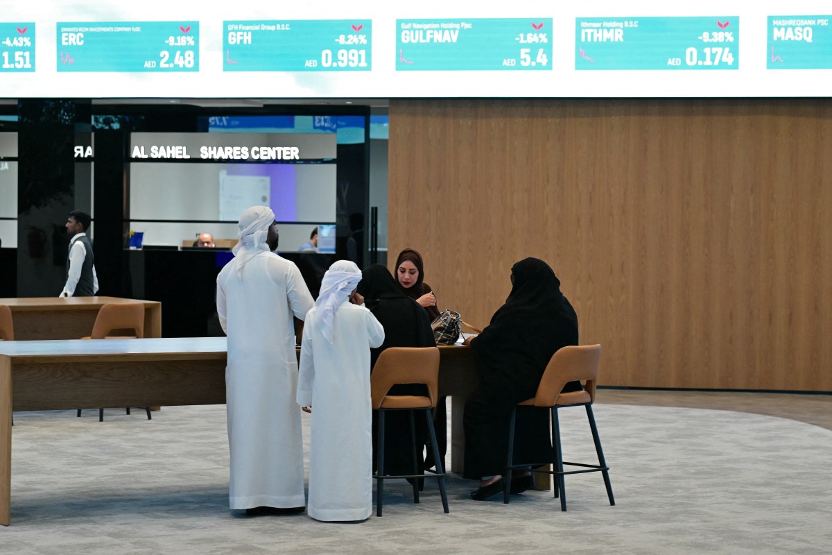 رجل يتصفح هاتفه أثناء جلوسه بالقرب من شاشة تعرض مؤشرات الأسهم في سوق دبي المالي في دبي. (أ ف ب)