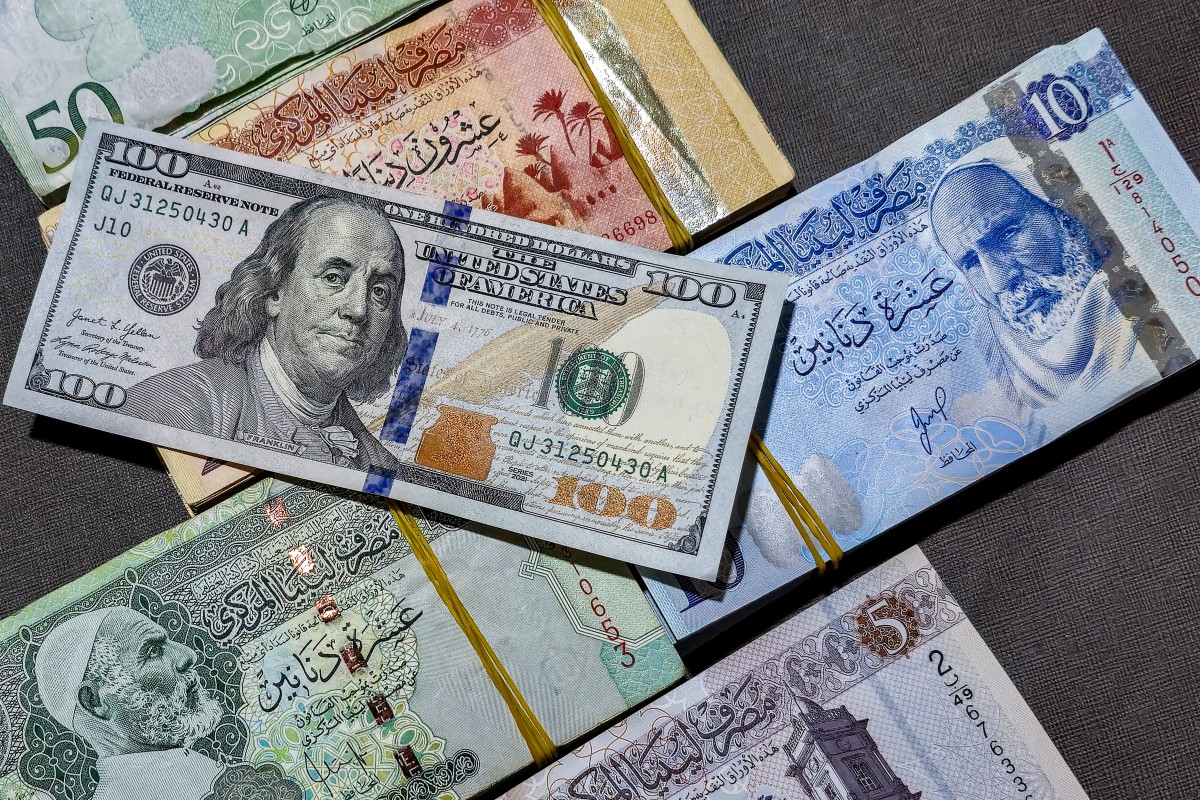 أكوام من أوراق الدينار الليبي من فئات عدة معروضة بجانب ورقة نقدية من فئة 100 دولار أميركي. (أ ف ب)