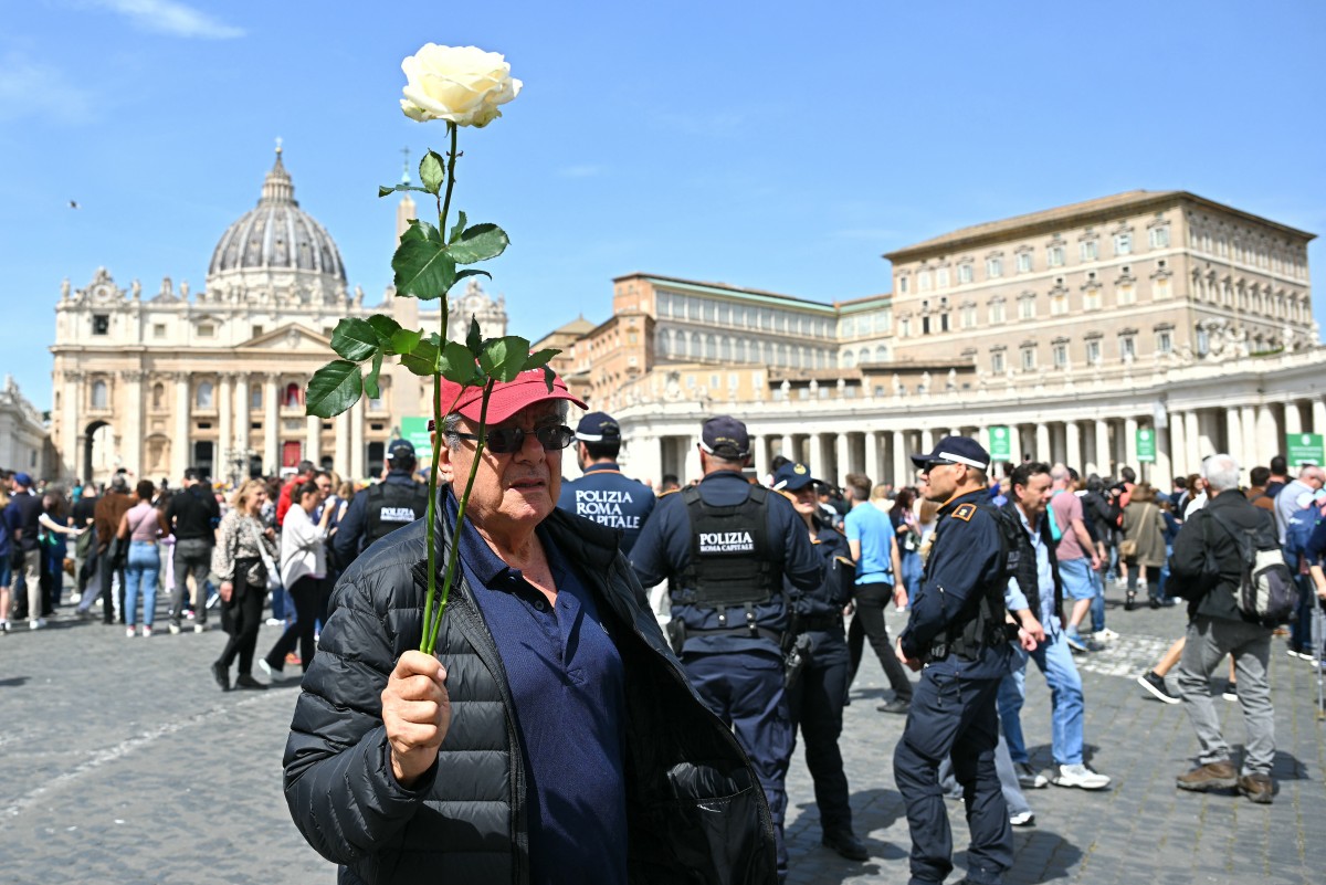 رجلٌ يحمل وردةً بيضاء يقف في ساحة القديس بطرس بعد وفاة البابا فرنسيس في الفاتيكان (أ ف ب).