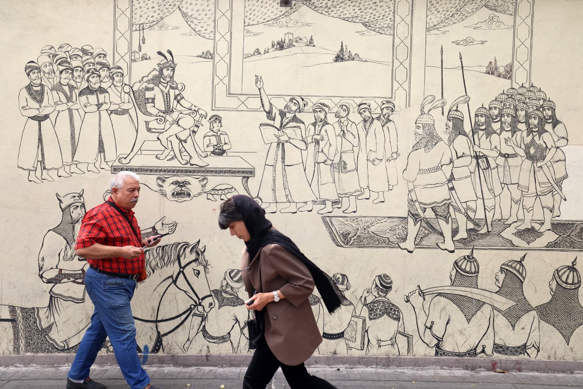 أشخاص يمرون أمام جدارية تُصوّر مشهدًا من الملحمة الوطنية الإيرانية