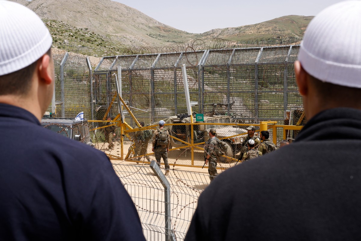 جنود إسرائيليون يقفون للحراسة بينما يتظاهر رجال دروز تضامناً مع الطائفة الدرزية السورية بالقرب من الجدار الحدودي في قرية مجدل شمس. (أ ف ب)