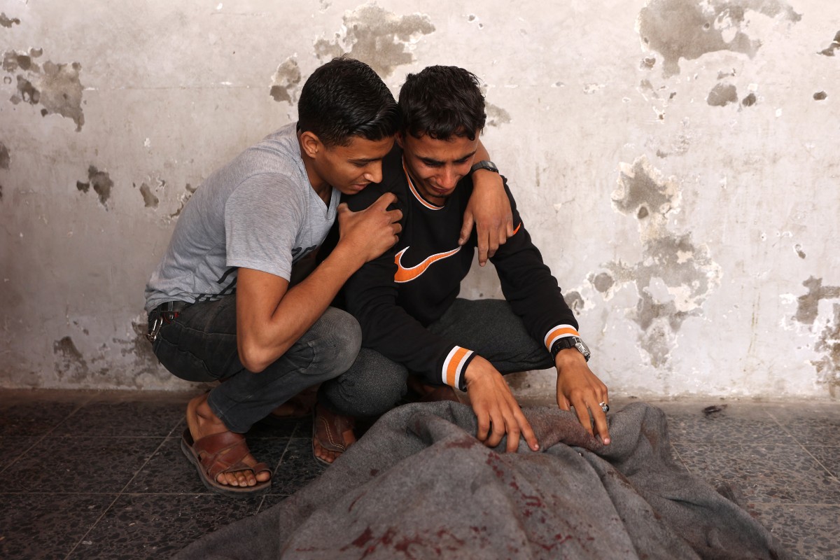 رجال فلسطينيون يبكون على جثة ملفوفة في بطانية في المستشفى الأهلي (أ ف ب)