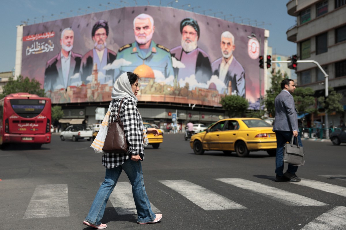 امرأة تمر أمام لوحة إعلانية تحمل صور قادة إيرانيين ولبنانيين مغتالين في ساحة انقلاب بطهران (أ ف ب)