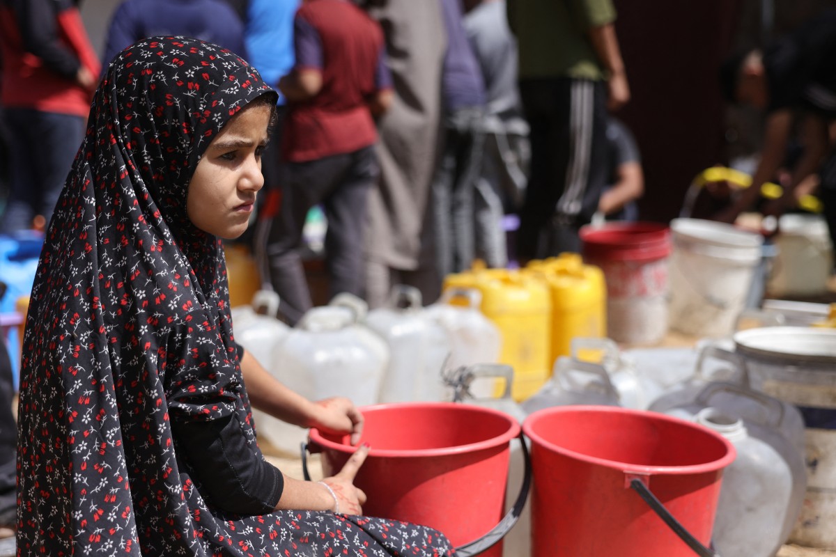 فتاة تجلس بجوار دلاء بلاستيكية بينما يجمع الفلسطينيون النازحون المياه في غزة. (20 أيار/مايو 2025 - أ ف ب)