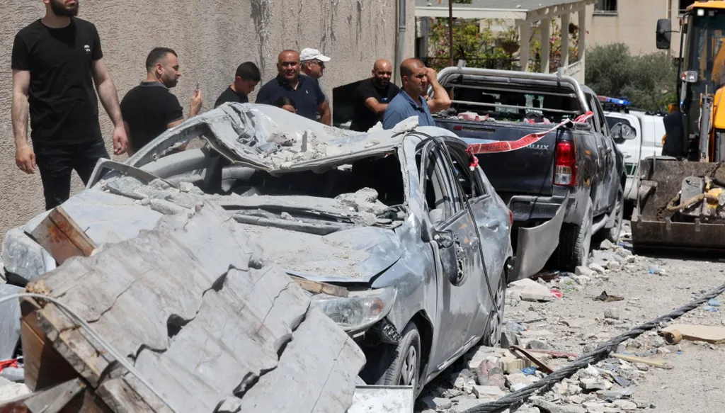 سكان يقفون بالقرب من سيارات متضررة بشدة في بلدة تمرا شمال إسرائيل، عقب هجوم صاروخي ليلي من إيران (أ ف ب)