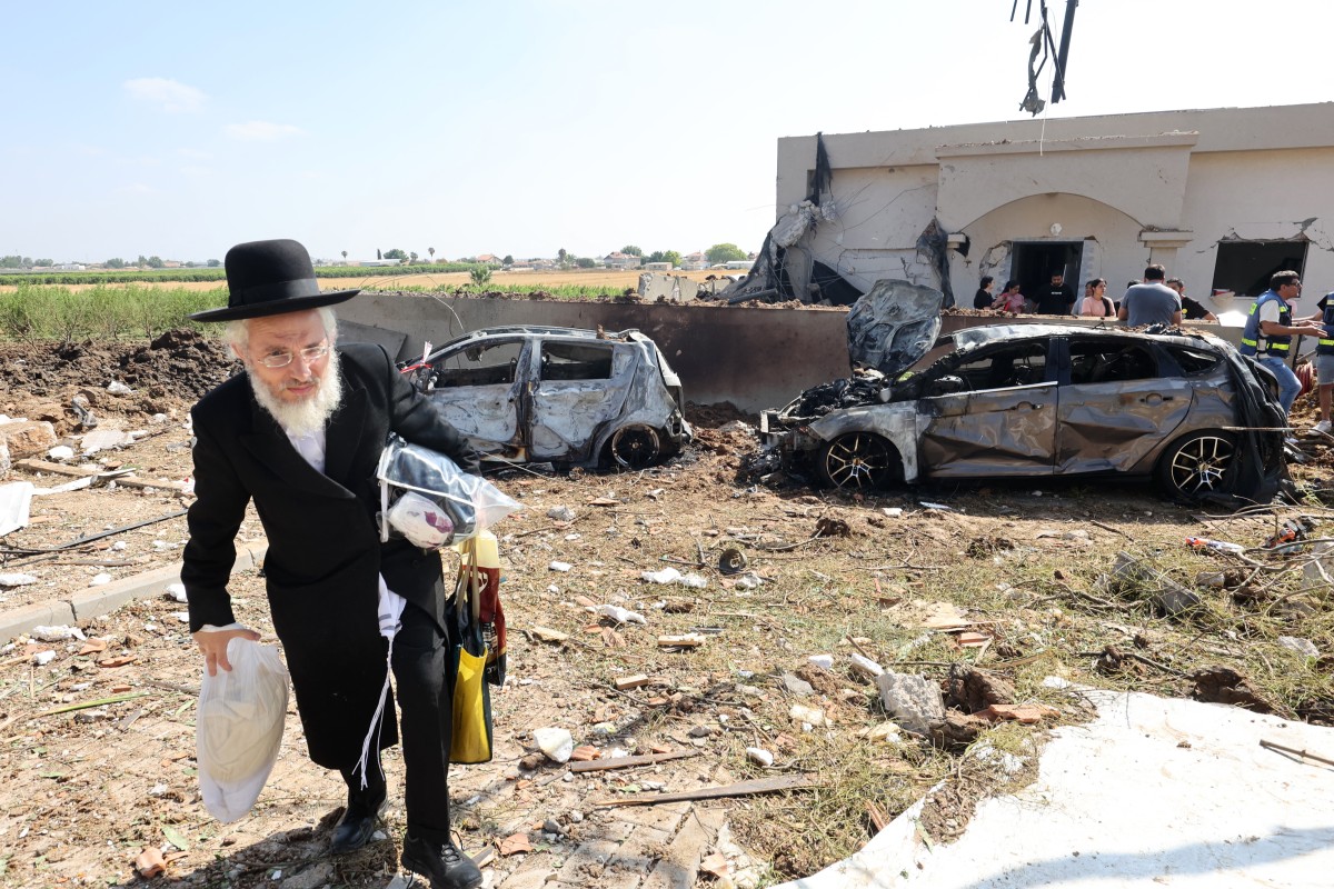 رجل يهودي متدين يحمل أغراضه في موقع الضربة الصاروخية الإيرانية في موشاف زافديئيل. (أ ف ب)