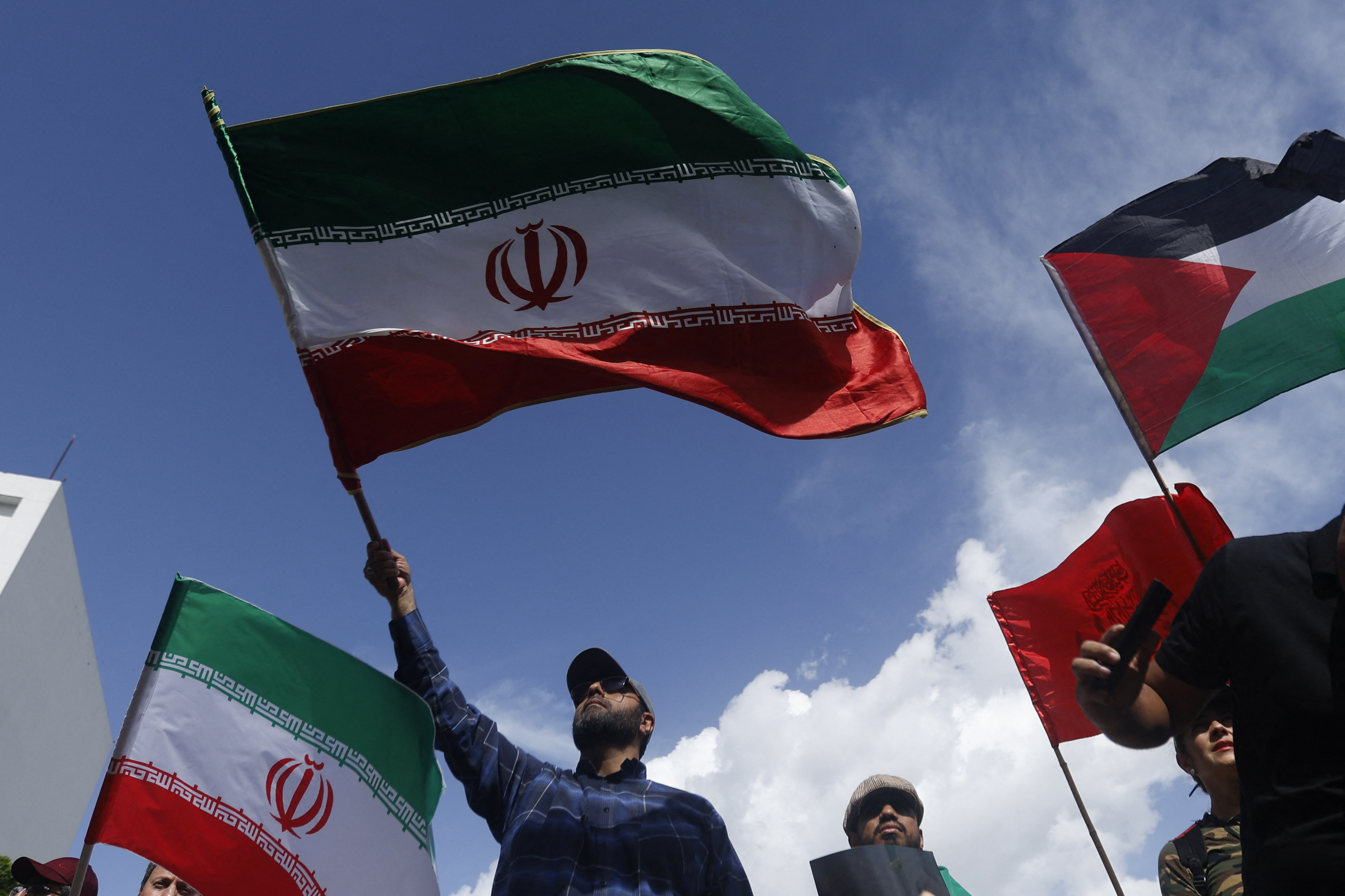 رجل يلوح بعلم إيراني خلال مظاهرة ضد الهجمات الإسرائيلية على إيران (أ ف ب)