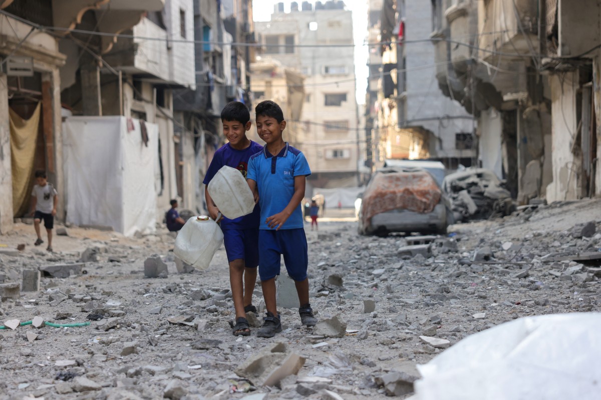 أطفال فلسطينيون يحملون حاويات مياه يسيرون على أنقاض مبنى استهدفه هجوم إسرائيلي في حي الشيخ رضوان في مدينة غزة، وسط قطاع غزة  (أ ف ب).