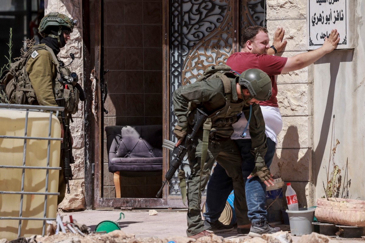 جنود الجيش الإسرائيلي يفتشون رجلاً فلسطينياً عند مدخل مخيم طولكرم بالضفة الغربية المحتلة (أ ف ب)