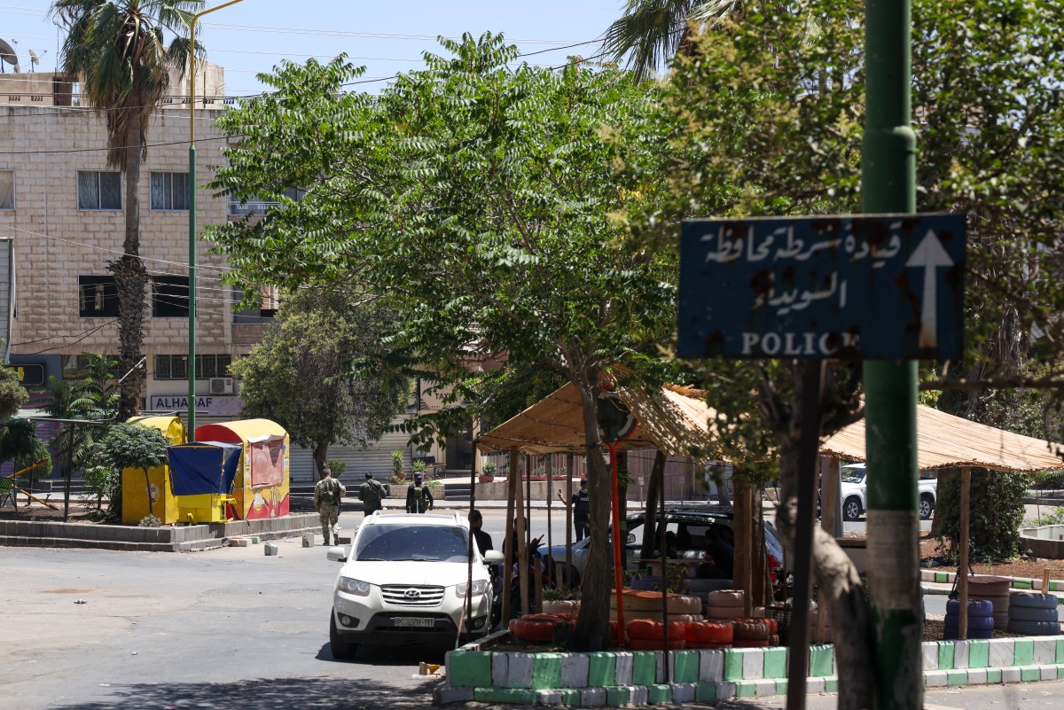 أحد أفراد قوات الأمن السورية يقف تحت لافتة في مدينة السويداء ذات الأغلبية الدرزية في 15 يوليو 2025 (أ ف ب)