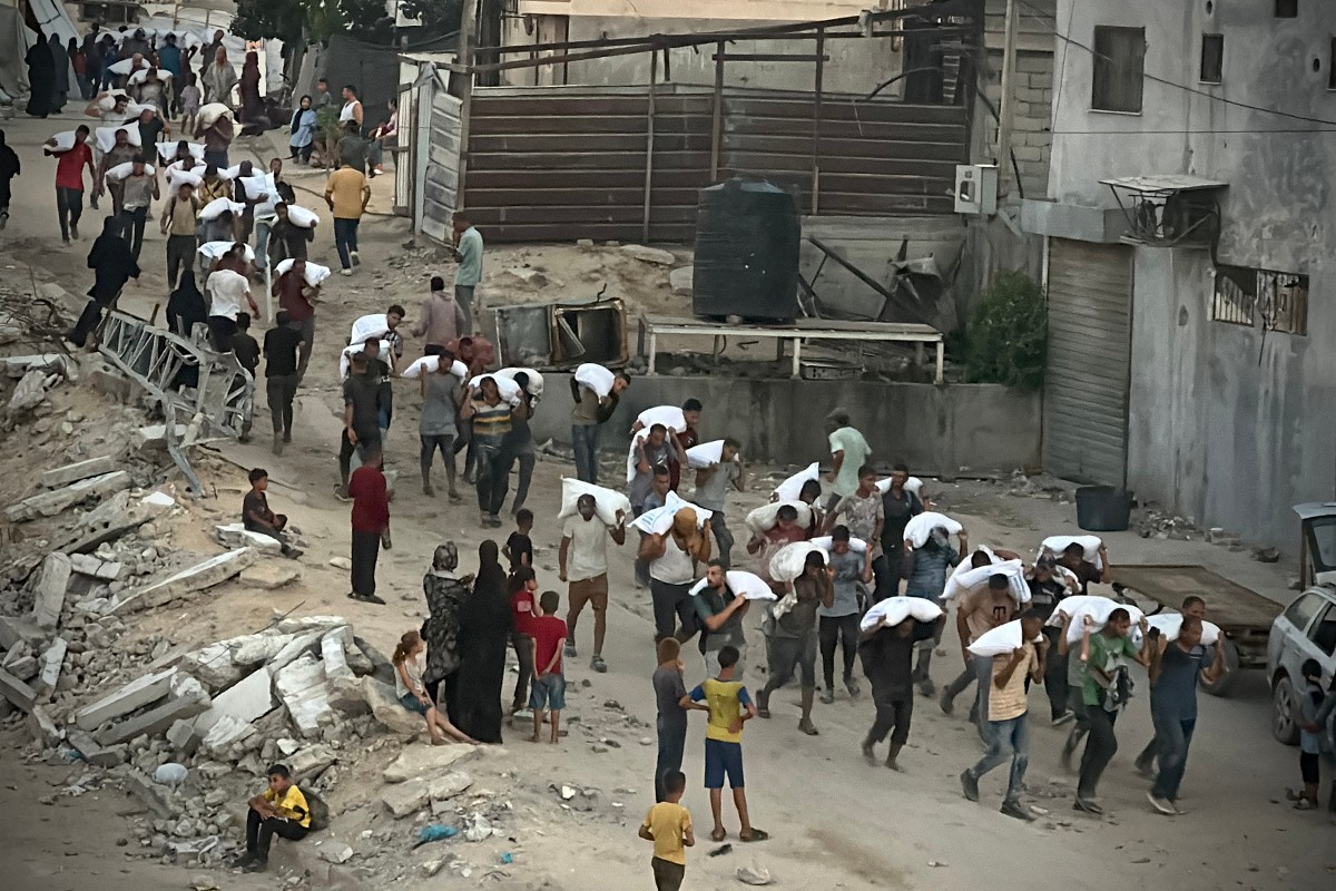 رجال يسيرون وهم يحملون أكياس الطحين في جنوب قطاع غزة، 22 يوليو، 2025. (Photo by AFP)