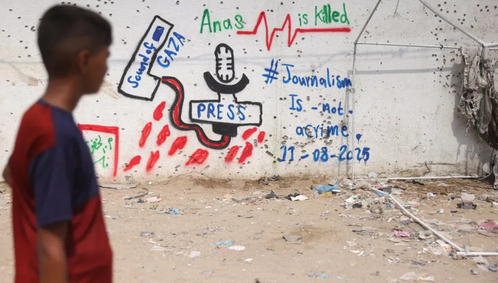 فلسطيني ينظر إلى كتابة على جدار في الموقع الذي دمرت فيه غارة إسرائيلية قاتلة خيمة تابعة لقناة الجزيرة وقتلت ستة صحافيين (أ ف ب).