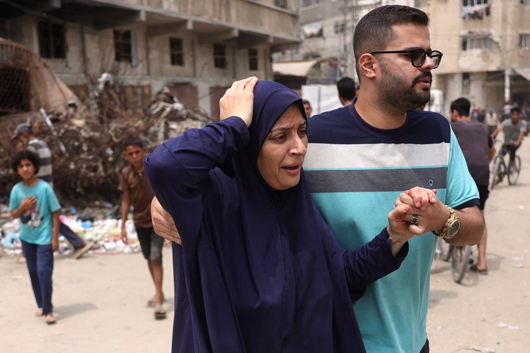 رجل فلسطيني يساعد امرأة مصابة على الفرار من موقع غارة إسرائيلية غرب مدينة غزة (أ ف ب)