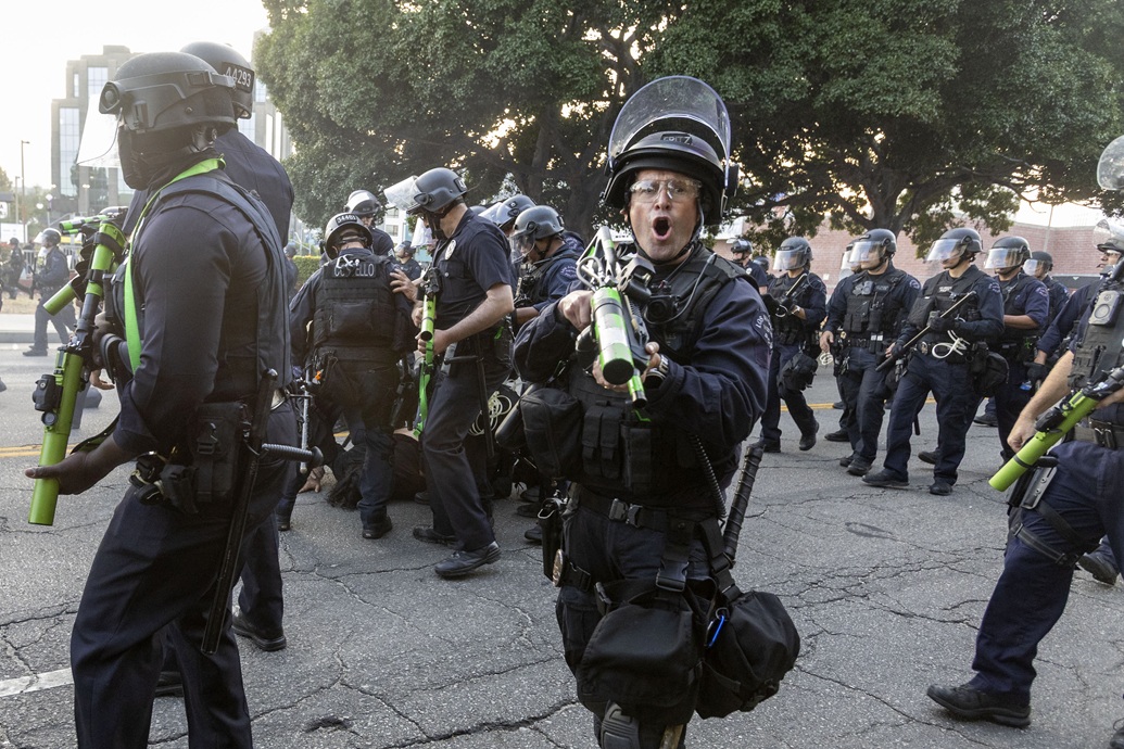 ضابط شرطة يرتدي ملابس مكافحة الشغب يطلق سلاحاً غير فتاك على المتظاهرين خلال مظاهرة أعقبت عمليات الهجرة الفيدرالية في لوس أنجليس (أ ف ب)