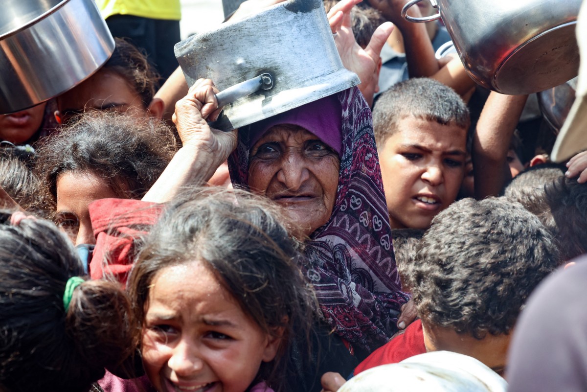 امرأة فلسطينية مسنة تنتظر مع أطفالها الحصول على الطعام من مطبخ خيري في خان يونس (أ ف ب)