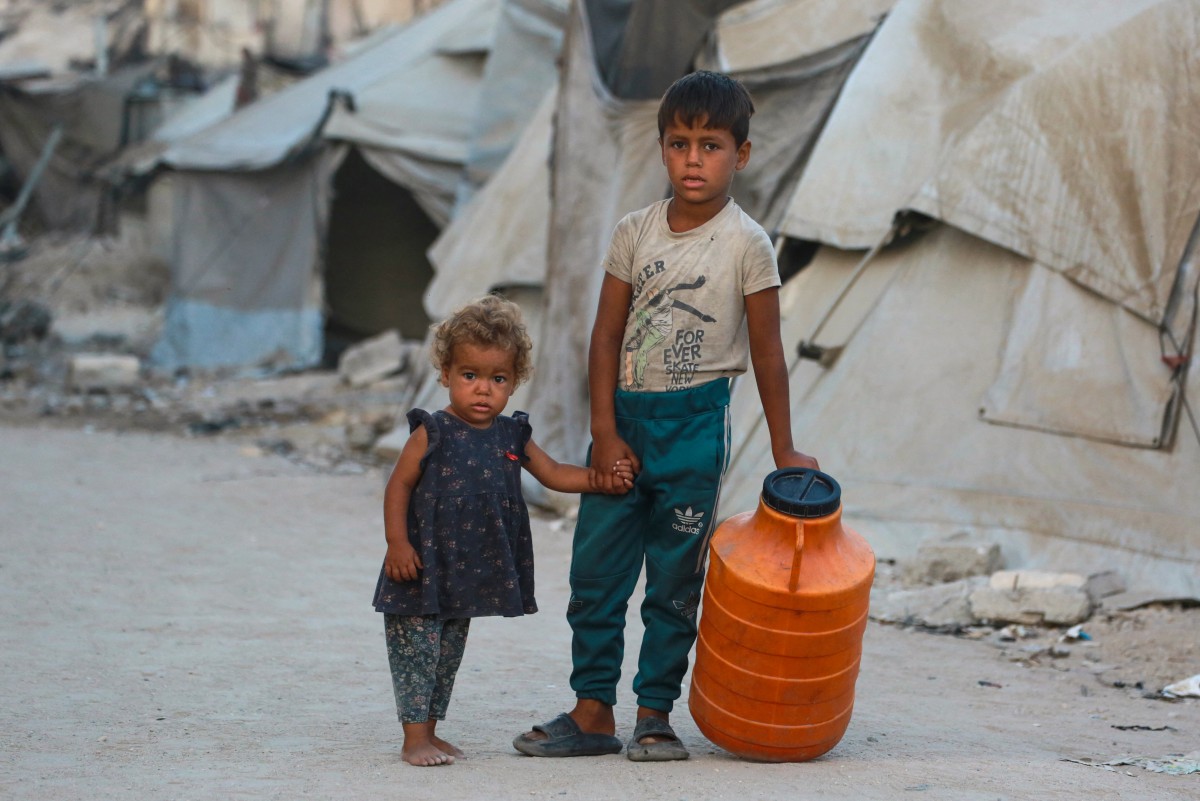 أطفال فلسطينيون يقفون بالقرب من خيام النازحين في مدينة غزة  (أ ف ب)