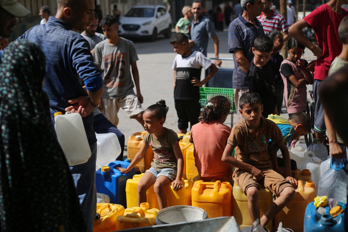 يجلس أطفال فلسطينيون على حاوياتهم أثناء انتظارهم للحصول على المياه في نقطة توزيع خيرية في مخيم النصيرات للاجئين في قطاع غزة  (أ ف ب)