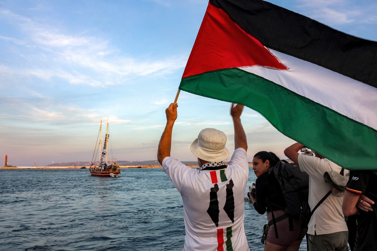 رجل يلوح بالأعلام الفلسطينية للنشطاء الآخرين والمدافعين عن حقوق الإنسان الذين يستقلون سفينة تغادر ميناء بنزرت شمال تونس للانضمام إلى آخر القوارب المشاركة في أسطول الصمود العالمي. (أ ف ب)
