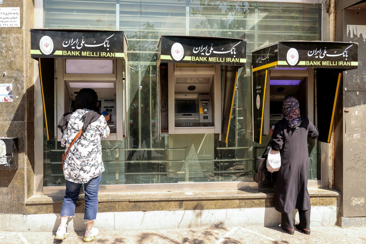 أشخاص يسحبون أموالاً من جهاز صراف آلي في العاصمة الإيرانية طهران  (أ ف ب).