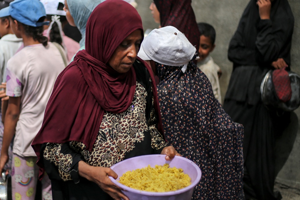 امرأة فلسطينية تحمل وعاء أرز بعد أن حصلت على حصة غذائية من مطبخ خيري في وسط قطاع غزة (أ ف ب)