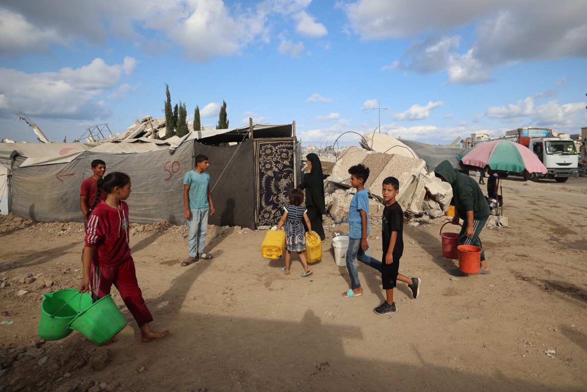يحمل الأطفال الدلاء والجراكن بينما يتجه الفلسطينيون النازحون إلى خزانات متنقلة لجلب مياه الشرب في مخيم البريج للاجئين في وسط قطاع غزة. (أ ف ب)