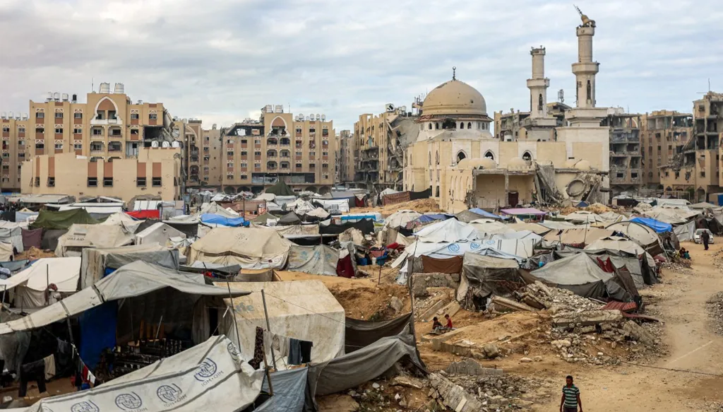 رجل يحمل صفائح بينما يسير أمام الخيام التي تؤوي النازحين بسبب الحرب التي تم نصبها بالقرب من مسجد الشيخ حمد بن خليفة آل ثاني في شمال غرب خان يونس، في جنوب قطاع غزة (أ ف ب)