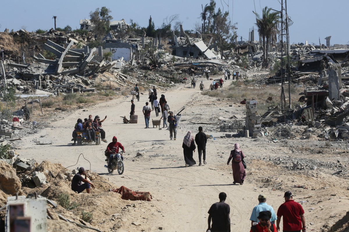 فلسطينيون نازحون يسيرون أمام المباني المدمرة أثناء عودتهم إلى منازلهم في منطقة الزهراء، شمال مخيم النصيرات للاجئين في وسط قطاع غزة، في 14 أكتوبر/تشرين الأول 2025 (أ ف ب)