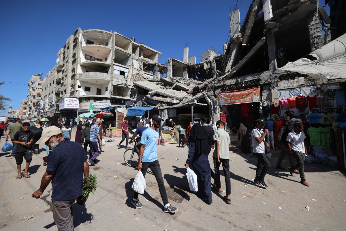 فلسطينيون يسيرون أمام مبنى مدمر في سوق موقت في مخيم النصيرات للاجئين، الواقع في وسط قطاع غزة. (أ ف ب)