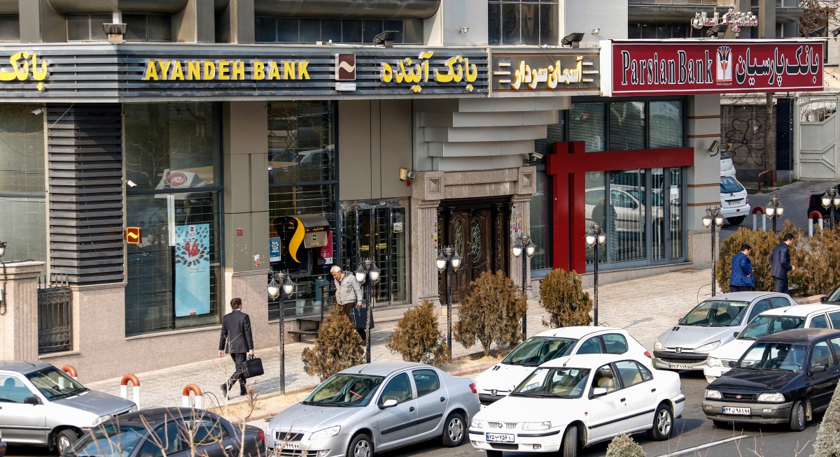 إيرانيون يمرون أمام فرع بنك أيانده (يسار) في العاصمة طهران (أ ف ب)