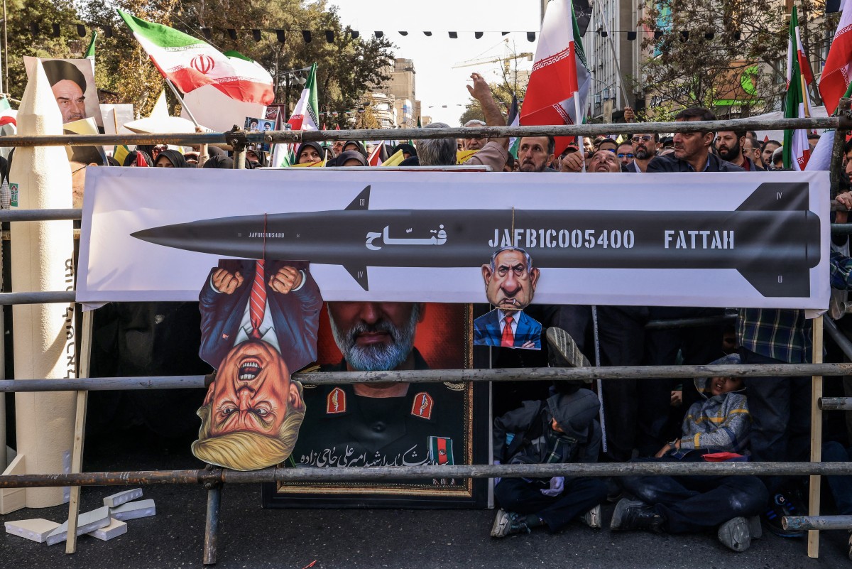 يتفاعل المتظاهرون بجوار لافتات تصور وجوه الرئيس الأميركي دونالد ترامب ورئيس الوزراء الإسرائيلي بنيامين نتنياهو خلال تجمع حاشد خارج السفارة الأميركية السابقة في طهران. (أ ف ب)