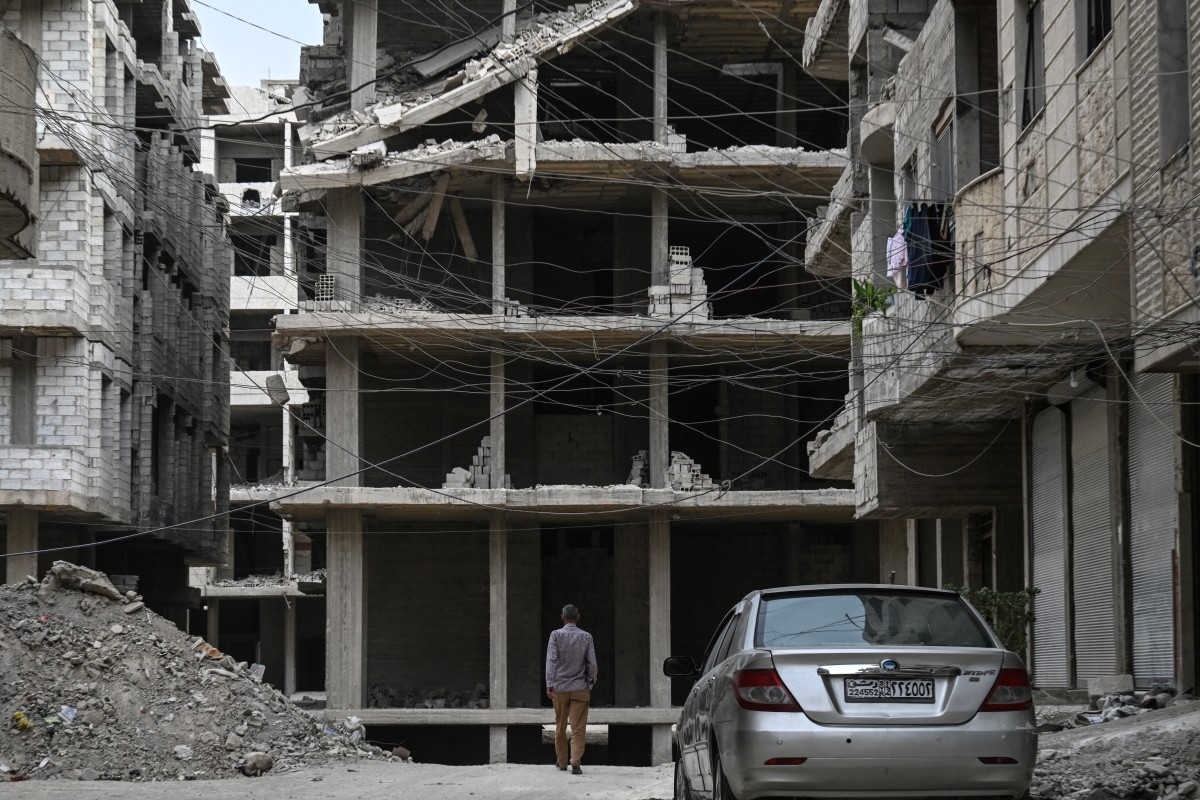 رجل يقف تحت شبكة من الكابلات الكهربائية المتشابكة الممتدة بين المباني المتضررة في منطقة عين ترما، على المشارف الشرقية للعاصمة دمشق (أ ف ب)