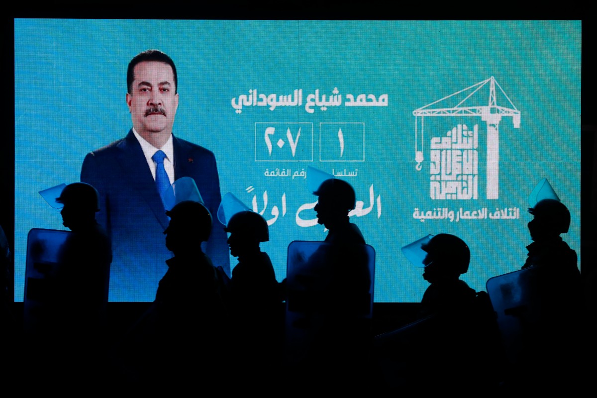 أفراد من شرطة مكافحة الشغب العراقية يمرون أمام شاشة تعرض صورة رئيس الوزراء العراقي الحالي محمد شياع السوداني خلال احتفالات أنصاره بعد الإعلان عن نتائج الانتخابات الأولية في بغداد (أ ف ب)