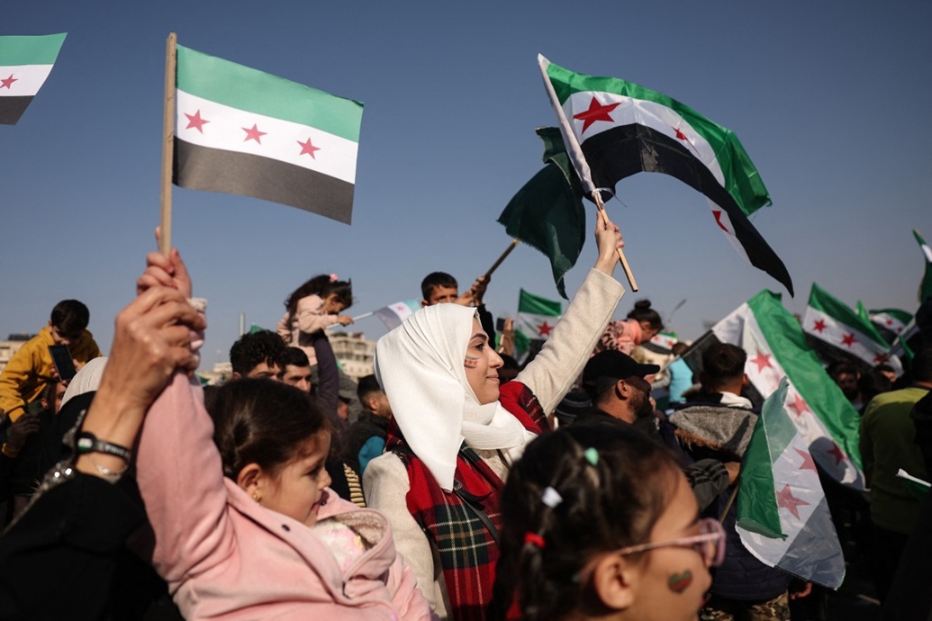 سكان يرفعون الأعلام السورية خلال احتفالات بمناسبة مرور عام على سقوط نظام الأسد (أ ف ب)