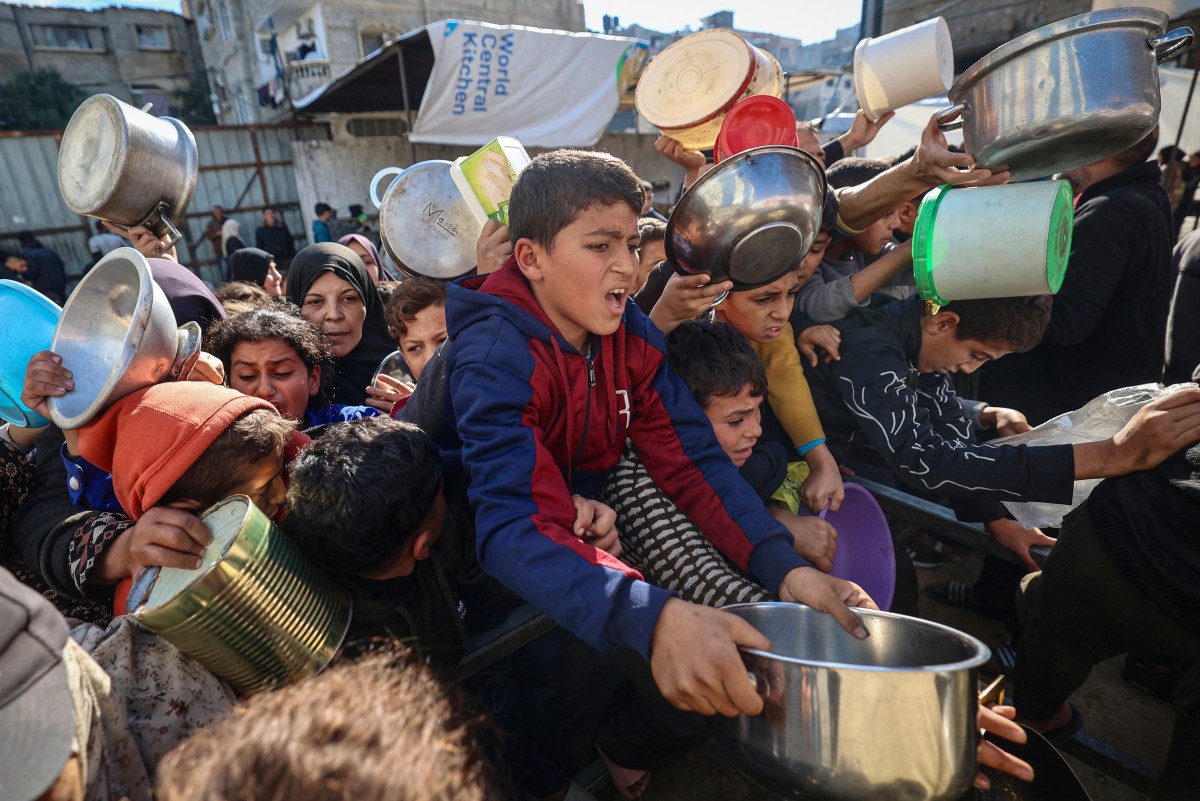 نازحون فلسطينيون يحاولون الحصول على حصص غذائية في مطبخ خيري بمخيم النصيرات للاجئين وسط قطاع غزة. (أ ف ب)