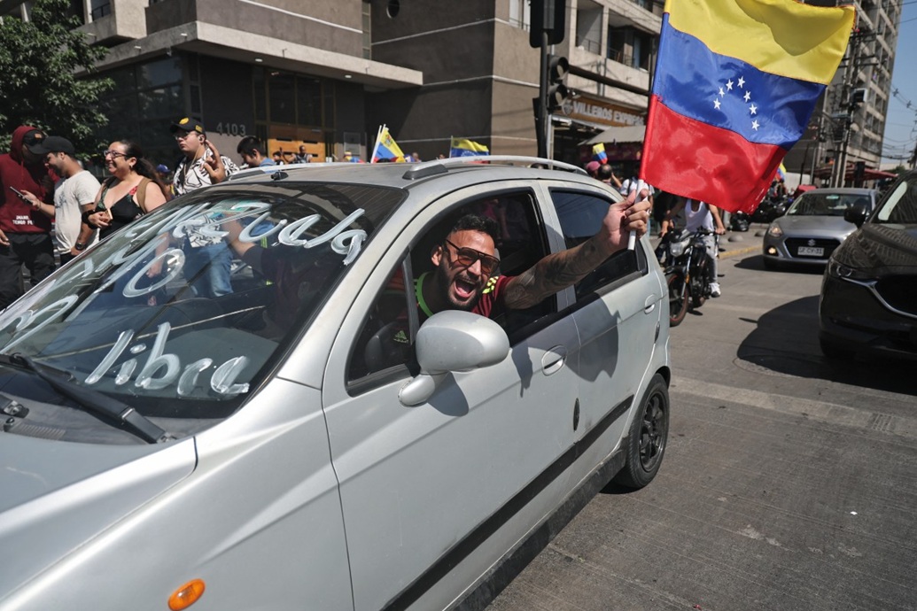 رجل فنزويلي يعيش في تشيلي يحتفل بالعلم الوطني وسيارته التي كُتب عليها ”فينزويلا حرة“ في سانتياغو (أ ف ب)