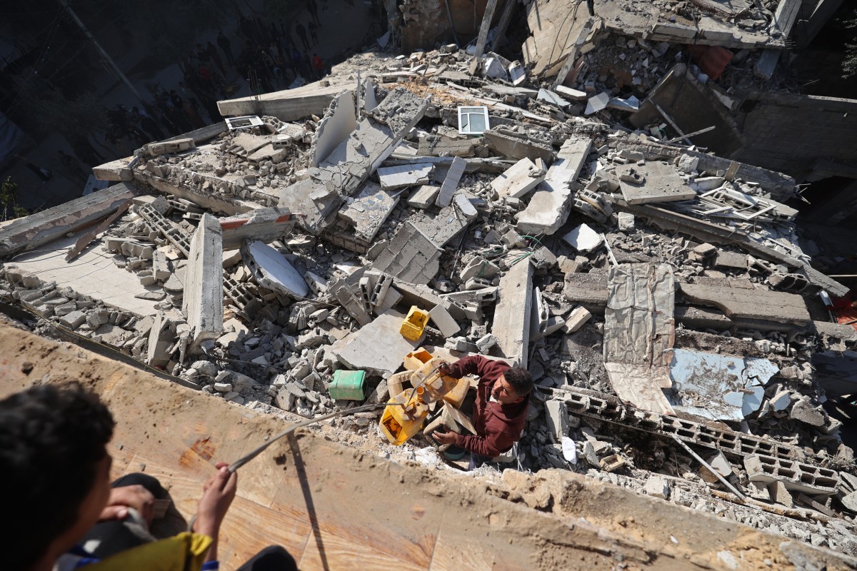 يحمل فلسطينيون علب بلاستيكية وسط أنقاض منزل منهار تضرر سابقاً جراء غارة إسرائيلية، وسط قطاع غزة. (أ ف ب)