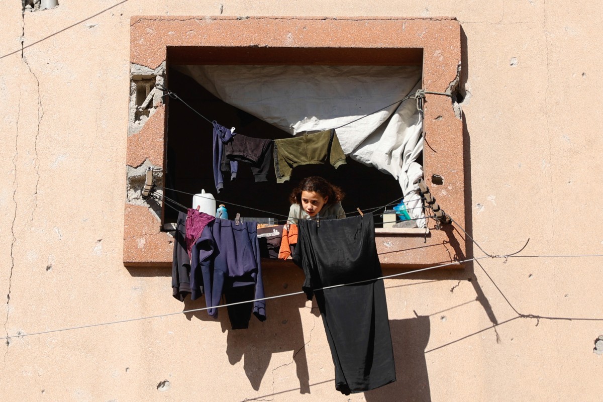 فتاة فلسطينية نازحة تنظر من نافذة مبنى تضرر خلال غارات عسكرية إسرائيلية سابقة، في مدينة غزة (أ ف ب). 