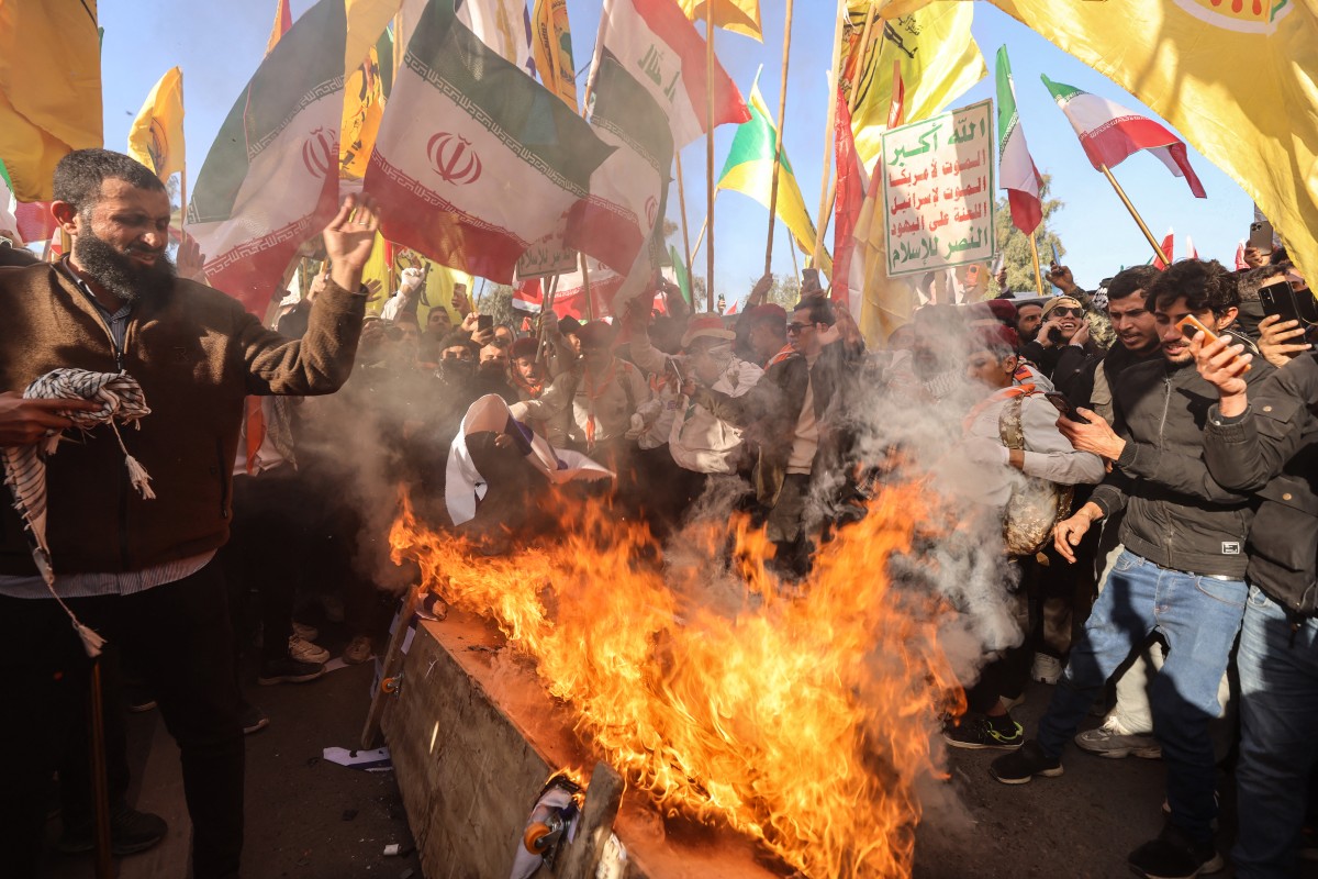 أنصار الفصائل المسلحة العراقية الموالية لإيران، إلى جانب متظاهرين آخرين، يحرقون أعلام الولايات المتحدة وإسرائيل خلال مظاهرة بالقرب من السفارة الإيرانية في بغداد. (أ ف ب)