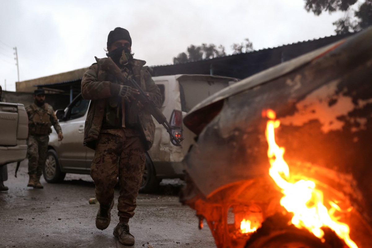 قوات وزارة الدفاع السورية تنظر إلى سيارة محترقة في مدينة الرقة الشمالية، على الضفة الشمالية لنهر الفرات. (أ ف ب)