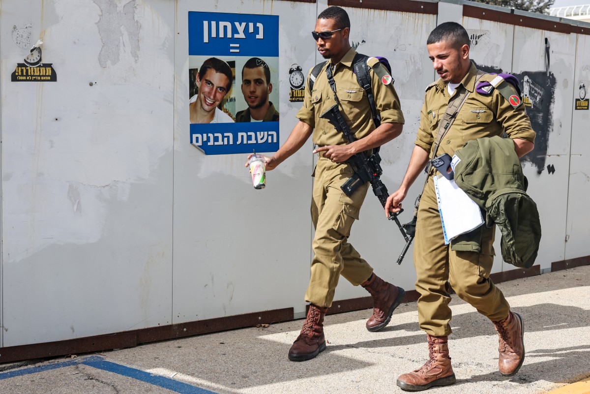 جنديان إسرائيليان يمران أمام ملصق لأسيرين كانا محتجزين سابقاً لدى حركة حماس في قطاع غزة. (أ ف ب)