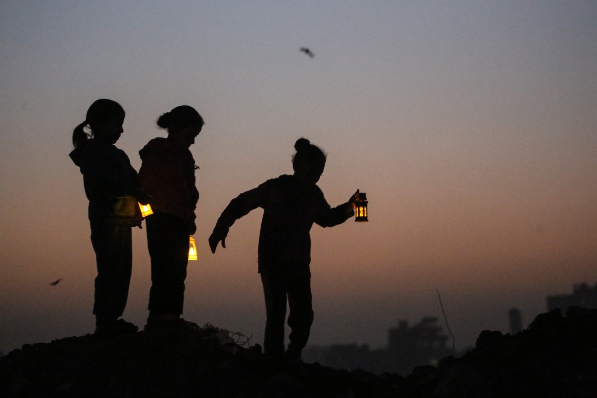 يلعب شبان فلسطينيون نازحون على أنقاض المباني المدمرة، حاملين فوانيس رمضان التي تستخدم كزينة، في مخيم البريج للاجئين وسط قطاع غزة. (أ ف ب)