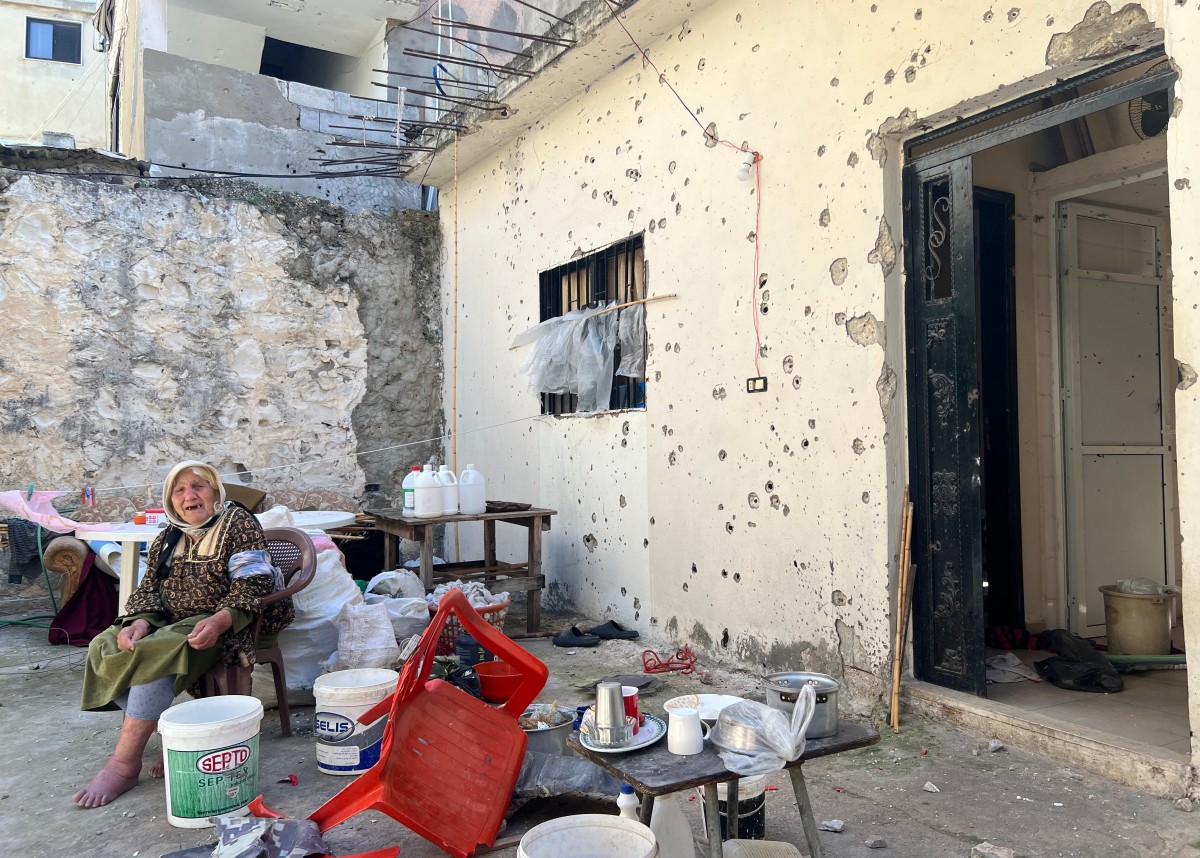 امرأة فلسطينية تجلس في الفناء الخارجي لمنزلها مقابل مبنى مدمر بعد يوم من الغارة الإسرائيلية على مخيم اللاجئين الفلسطينيين في عين الحلوة (أ ف ب)