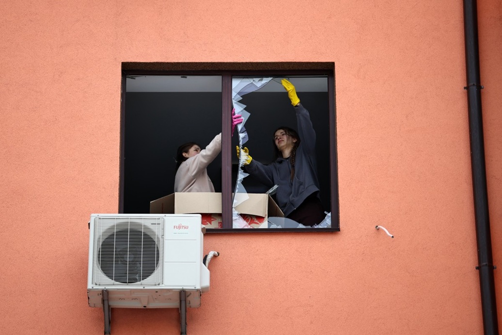 سكان محليون يزيلون شظايا زجاجية من نافذة مكسورة في مبنى سكني عقب غارة جوية في سوفييفسكا بورشاجيفكا، بمنطقة كييف (أ ف ب)